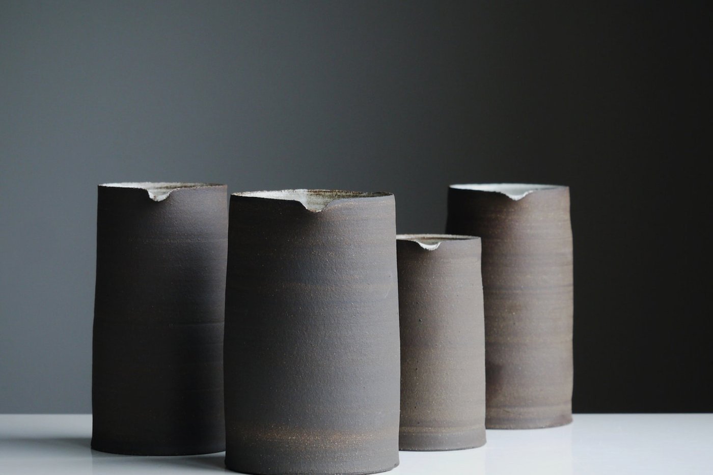 Four handmade stoneware jugs against a dark wall