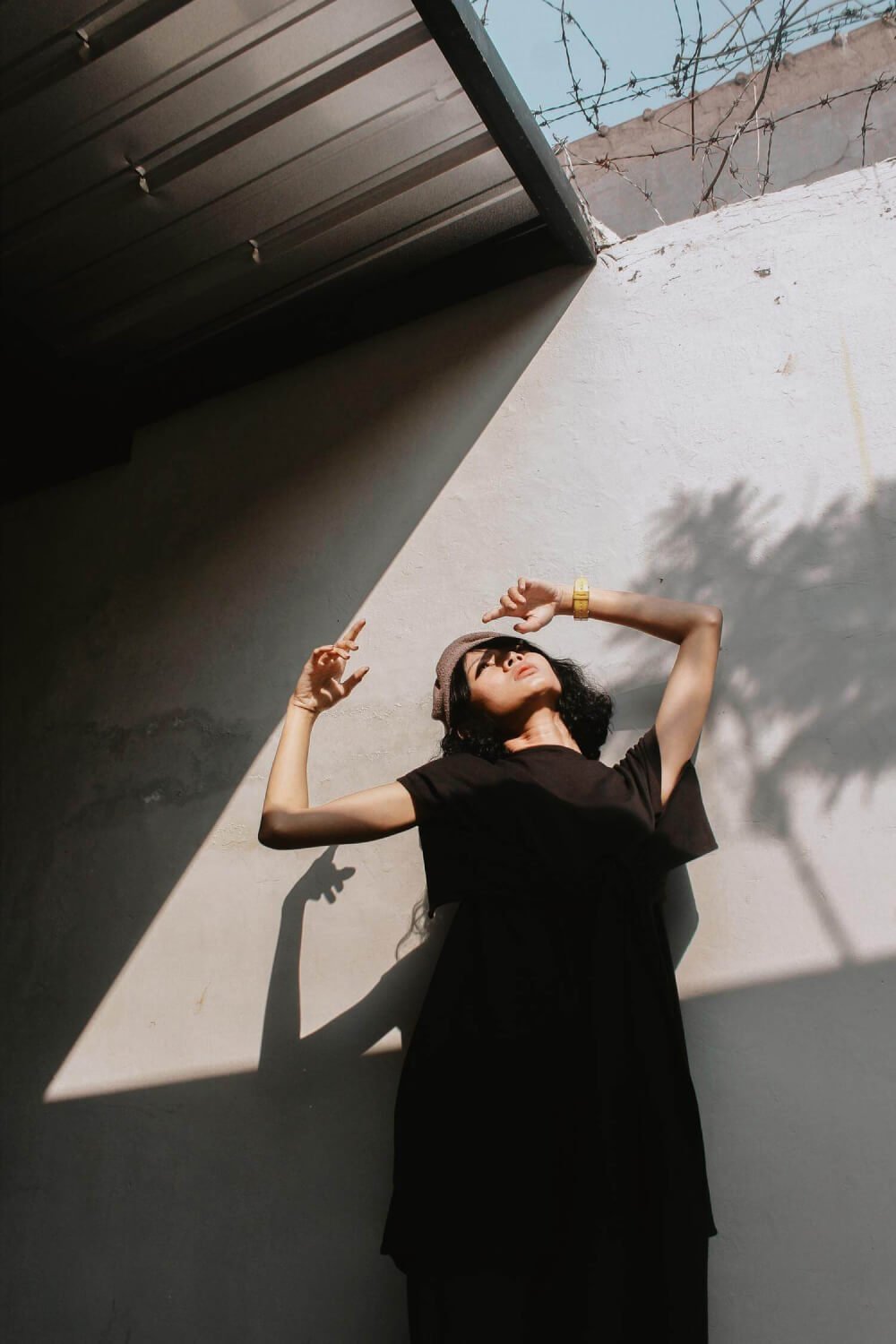 Woman in black posing in sunlight and shadow against a white wall